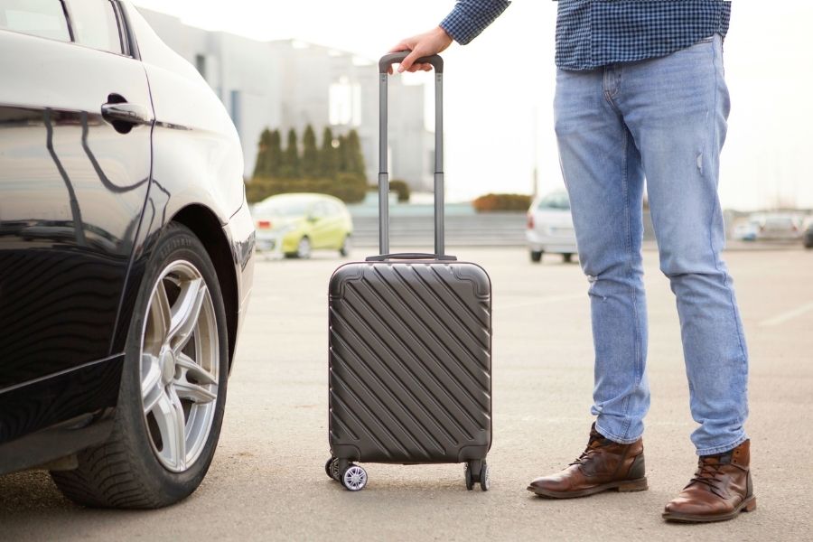 Woman arriving at airport smiling and waving, luggage in hand, ready to pick up her rental car at Cagliari Airport
